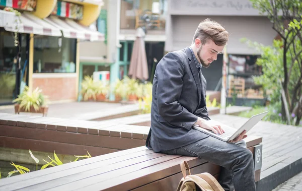 Yönlendirme ve ilham arayan mutlu genç iş adamının portresi kahve dükkanında dizüstü bilgisayarla oturuyor.