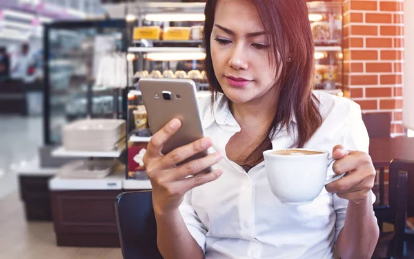 Las mujeres de Asia que beben café y miran su teléfono celular en la sa — Foto de Stock