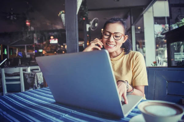 快乐的亚洲女人坐在咖啡店里 用笔记本电脑和手机 — 图库照片