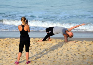 Sahilde yoga yapan genç bir kadın.