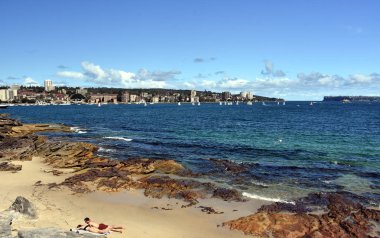 Manly, Avustralya - 4 Şubat 2018. Yaz aylarında güneşli bir plaj Delwood. Kuzey baş ve Güney kafa arka planda vardır. Yelkenli teknelerde Sydney Harbour.