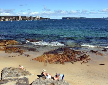 Manly, Avustralya - 4 Şubat 2018. Yaz aylarında güneşli bir plaj Delwood. Kuzey baş ve Güney kafa arka planda vardır. Yelkenli teknelerde Sydney Harbour.