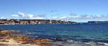 Manly, Avustralya - 4 Şubat 2018. Yaz aylarında güneşli bir plaj Delwood. Kuzey baş ve Güney kafa arka planda vardır. Yelkenli teknelerde Sydney Harbour.