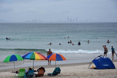 Coolangatta, Avustralya - 26 Aralık 2017. Rahatlatıcı ve gökkuşağı kumsalda güneşlenme insanlar. Gökkuşağı renkli şemsiyeler. Gold Coast manzarası içinde belgili tanımlık geçmiş.