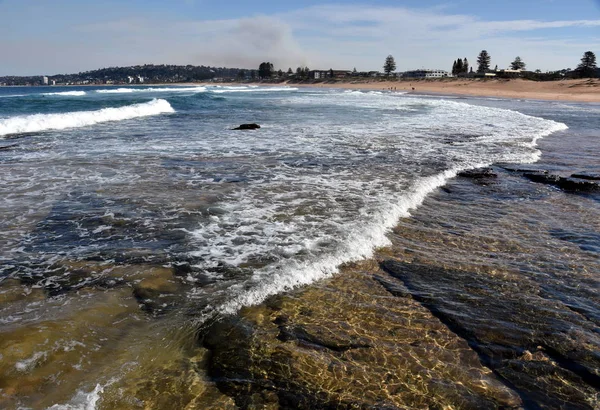 Waves crash and the water flows onto the rock shelf at Narrabeen beach (Sydney, Australia)