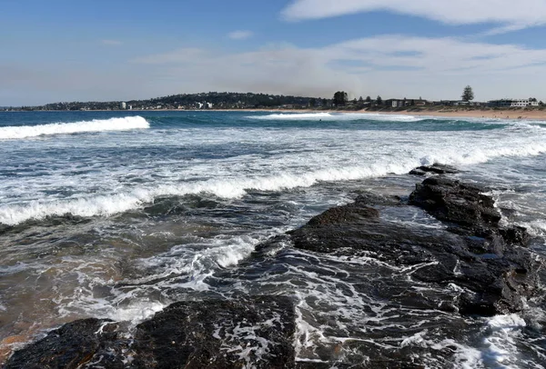 Waves crash and the water flows onto the rock shelf at Narrabeen beach (Sydney, Australia)