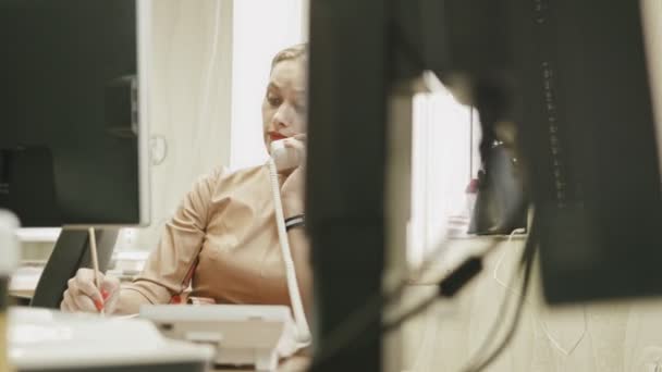 Attractive young woman - Charming office working answering the phone in her office in front of computer, dolly shot — Stock Video