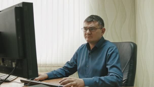 Trabajador de oficina en gafas delante de la computadora de escritorio, dolly shot — Vídeos de Stock