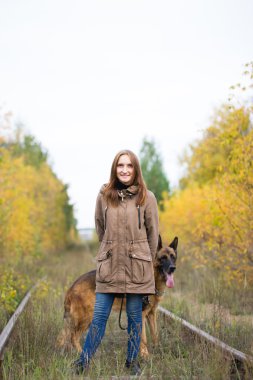 Young cute woman with german shepherd dog posing in autumn forest near rail way