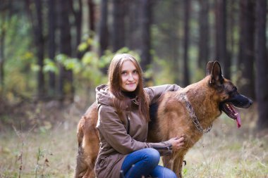 Young attractive woman posing with German Shepherd dog and smiling outdoors in the autumn park, close up