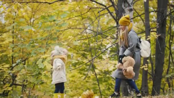 Мать и ее дочь маленькая девочка, гуляющая в осеннем парке - играть с медведем Тедди — стоковое видео