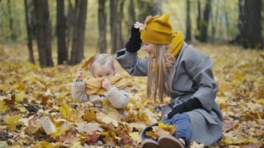 Anne ve kızı küçük kız bir sonbahar park - anne ve çocuk yürüyüş var eğlenceli ve gömülü sarı yaprakları