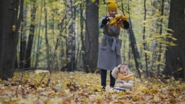 Anne ve kızı küçük kız bir sonbahar park - anne ve çocuk yürüyüş var eğlenceli ve sarı yaprakları ile oynarken