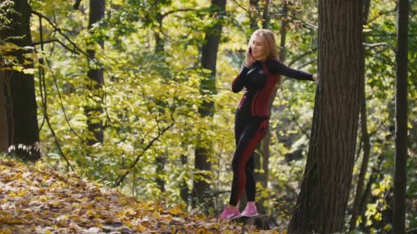 Mujer joven y deportiva hablando por teléfono celular en el parque de otoño al aire libre — Vídeo de stock