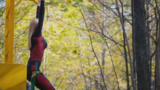 年轻的健身女性模型运动在草甸在秋天公园，体育户外活动概念 — — 在单杠上练习 — 图库视频影像