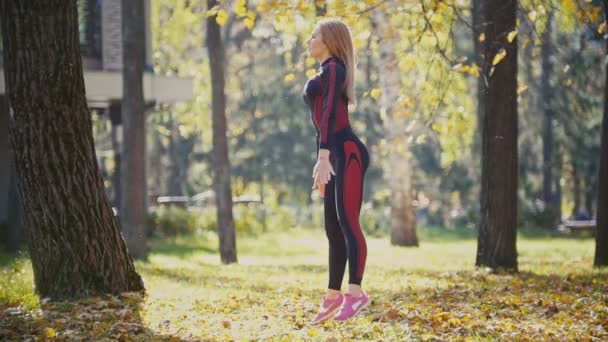 Sexy aantrekkelijke vrouwelijke blonde bikini-fitness model die zich uitstrekt in het najaar park op grond overdekte gele bladeren in slow motion — Stockvideo