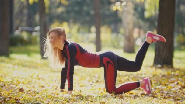 Sexy atraktivní žena blond bikini fitness model táhnoucí se v podzimním parku na půdě zahrnuty žluté listy - zvedání nohou — Stock video