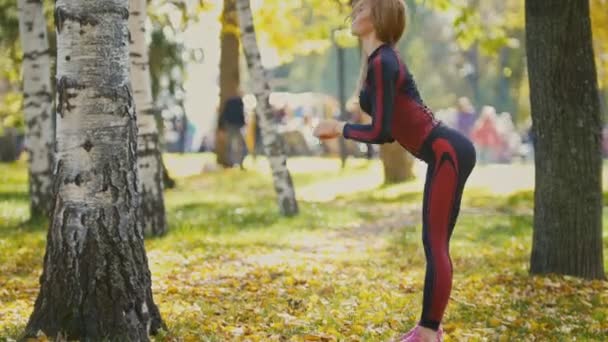 Sexy Attractive female blonde bikini-fitness model stretching in the autumn park on ground covered yellow leaves - the tilt of the body — Stock Video