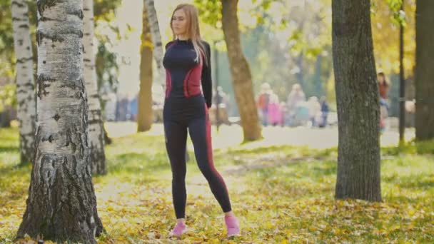 Sexy atraktivní žena blond bikini fitness model táhnoucí se v podzimním parku na zem pokrytá žluté listy - natahování zbraně — Stock video