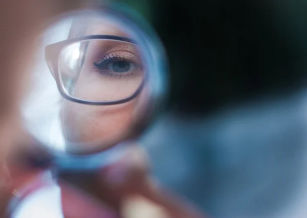 Mujer joven en gafas mirando en espejo cosmético, de cerca — Foto de Stock