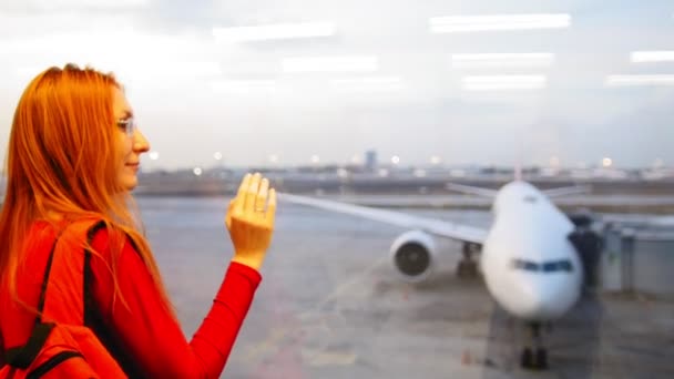Молода приваблива жінка з рудим волоссям і окулярами дивиться на літаки в аеропорту злітно-посадкової смуги — стокове відео
