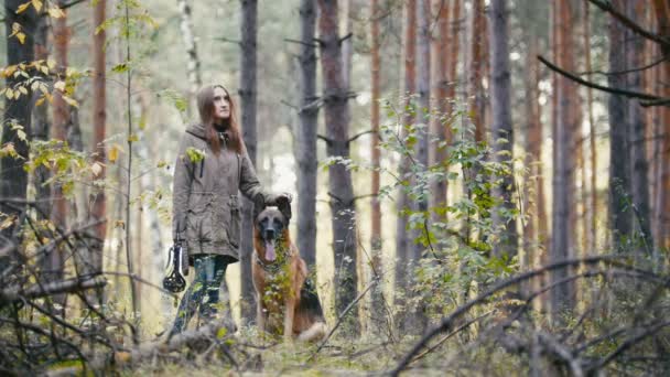 年轻漂亮的可爱的女人走在秋天的树林，她站在一片空地，抚摸着他的狗的女孩的宠物-德国牧羊犬- — 图库视频影像