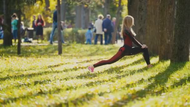 Фітнес-жіноча силова підготовка робить тренування в парку. Вмістити біла спортивна дівчина займається своїм тілом в сонячну осінь — стокове відео