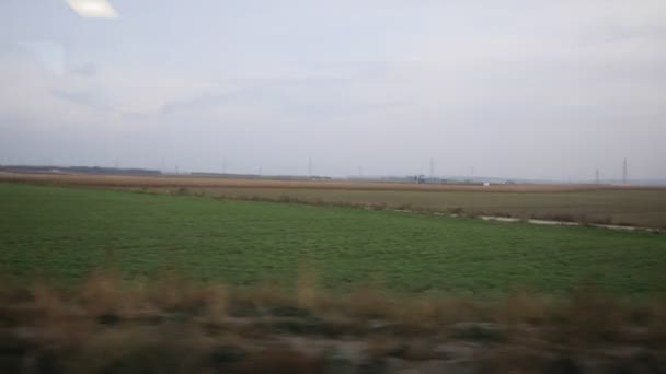 View from train - High voltage pylons, meadows, wind energy turbine — Stockvideo