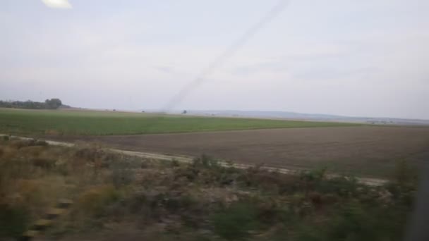 Vista desde el tren - turbina de energía eólica en segundo plano, agrícola, campo — Vídeos de Stock