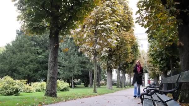 Красивая молодая женщина с рыжими волосами и очками ходит по парку и разговаривает по телефону - Бургхаус, Вена, широкий угол — стоковое видео