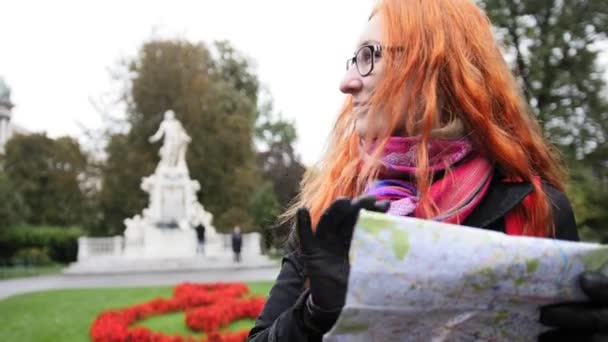 Yong kvinna turist med rött hår och glasögon tittar karta i Burggarten, Wien, Österrike — Stockvideo