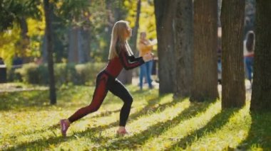Fitness kadın vücut geliştirme egzersiz güneşli sonbahar Parkı'nda yapıyor. Onun vücut - ağız kavgası, yan görünüm yapıyor beyaz sportif kız uygun