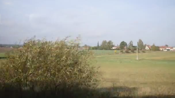 View from train window - rural landscape of farms, fields, trees sunny day — ストック動画