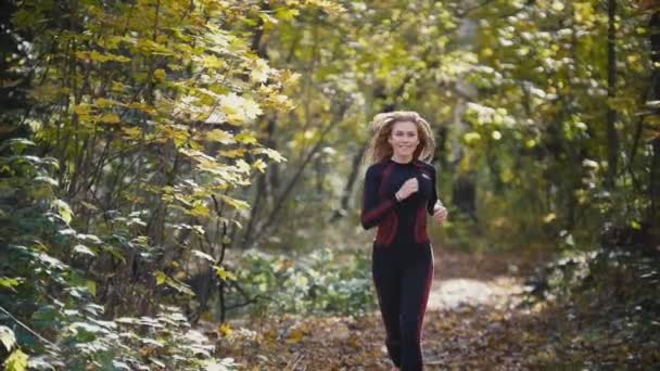 Jeune athlète féminine active faisant de l'exercice en plein air parc d'automne. Fille souriante, cheveux ondulés, Femmes en bonne santé, ralenti — Video