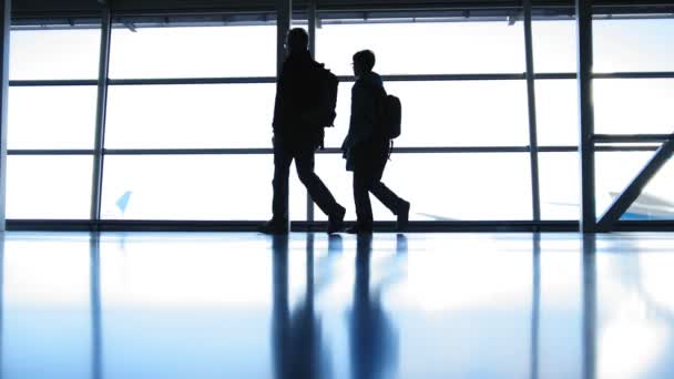 Dos viajeros que van en el aeropuerto frente a la ventana frente a la pista, silueta — Vídeos de Stock