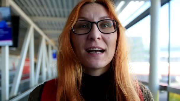 机场-幸福的女人，与红色的头发和眼镜乘坐自动扶梯 — 图库视频影像