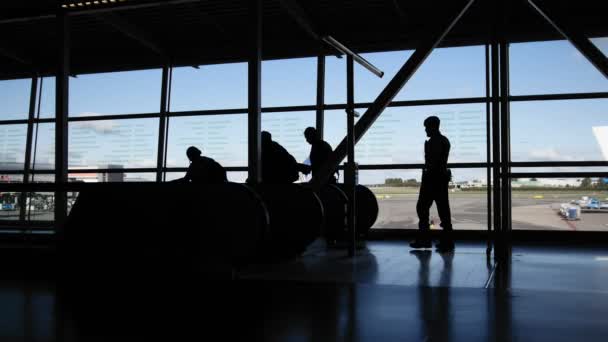 Viajeros en el aeropuerto caminando a las salidas en escaleras mecánicas delante de la ventana, silueta — Vídeos de Stock