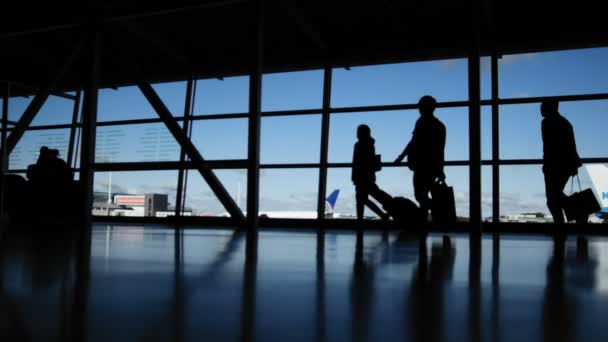 Viajeros con maletas y equipaje en el aeropuerto caminando a las salidas frente a la ventana, silueta — Vídeo de stock