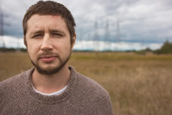 Portret van volwassen sterke man met baard op herfst weide, energie pylonen op achtergrond — Stockfoto