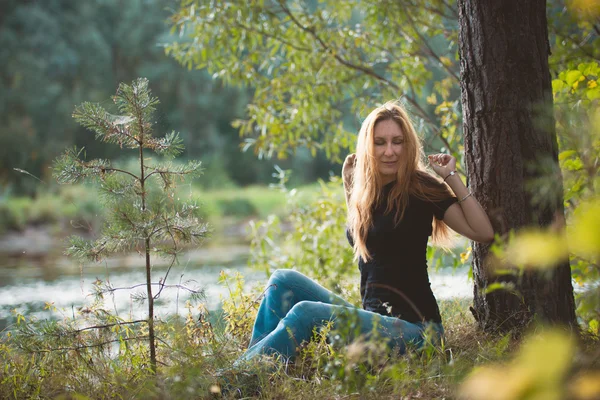 Young beautiful woman sitting near forest river and stretching, Russia, Siberia — Stock Photo, Image