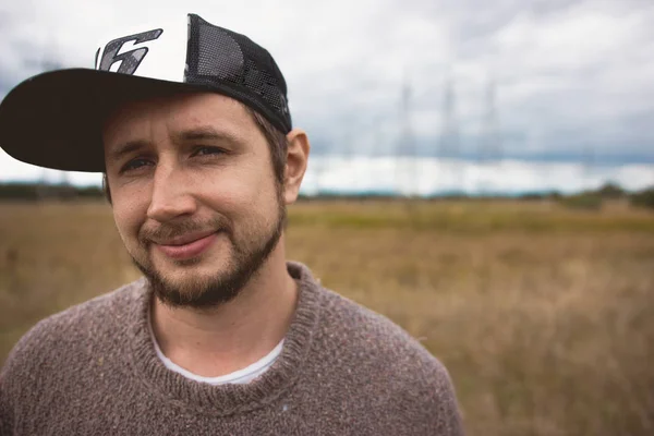 Portret van volwassen moedige jonge man op weide, macht masten op de achtergrond — Stockfoto