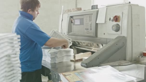 Εργαζόμενος σε μπλε σακάκι εργαζόμενος βάζει το χαρτί στο μηχάνημα λαιμητόμος κόφτης σε εκτύπωση εργοστάσιο, Ολισθητής — Αρχείο Βίντεο