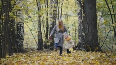 Onun annesi yürüyüş sonbaharda ormanlar ve tekme ile küçük kızı sarı yapraklar
