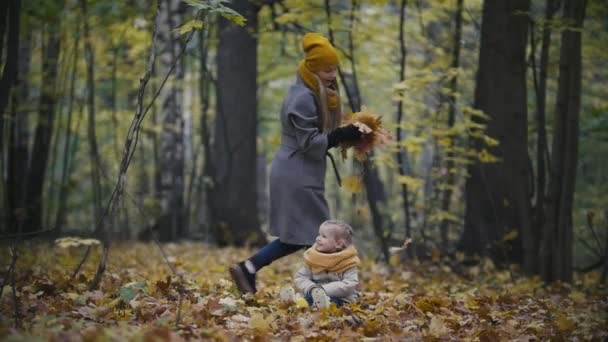 Счастливая семейная концепция - маленькая дочка с мамой играет с желтыми листьями в осеннем лесу, замедленном движении — стоковое видео