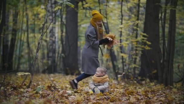 Concetto di famiglia felice - figlioletta con la madre gioca con foglie gialle nella foresta autunnale, slow-motion — Video Stock