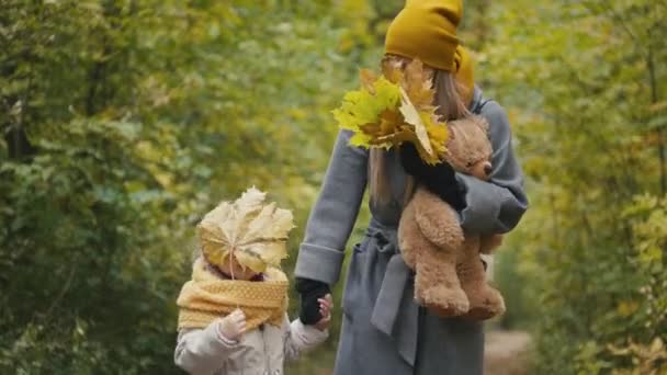 Filhinha com sua mamãe andando no parque de outono - brinca e se esconde atrás das folhas — Vídeo de Stock
