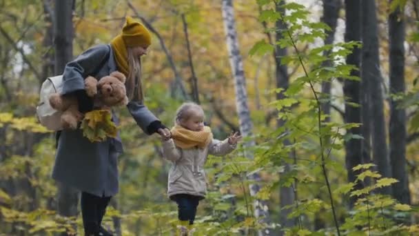 Маленька донька з мамою гуляє в осінньому парку - грає в листя — стокове відео