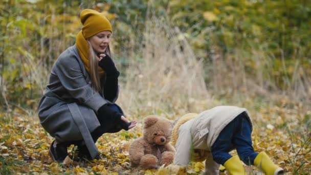 Gelukkige familie concept - dochtertje met haar mama en Taddy beer speelt met gele bladeren in de herfst park — Stockvideo