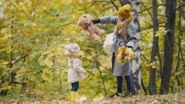 Neşeli küçük kızı ile onu anne ve Teddy Bear sonbahar parkta yürüyor