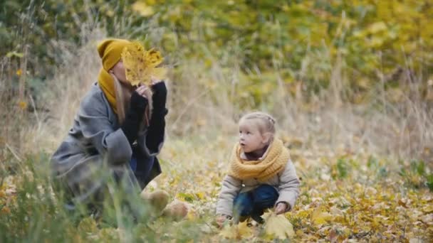 Blonde kleine Tochter mit Mama spaziert im Herbstpark - lustig sein und Blätter sammeln — Stockvideo